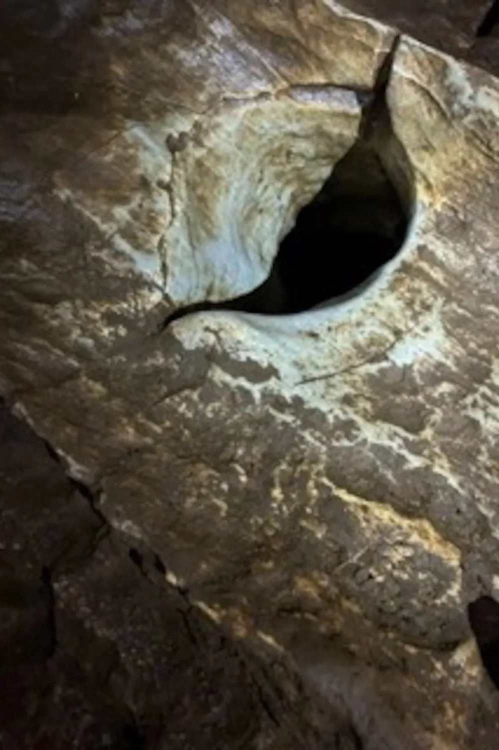 A small half-moon shaped hole, the entrance to the Womb Room in California Caverns.