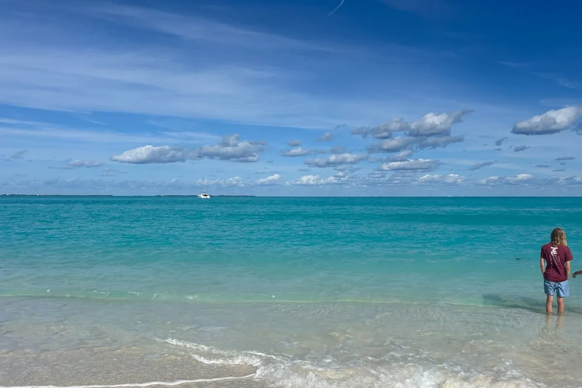 a boy stands in clear blue water at a beach in Treasure Cay