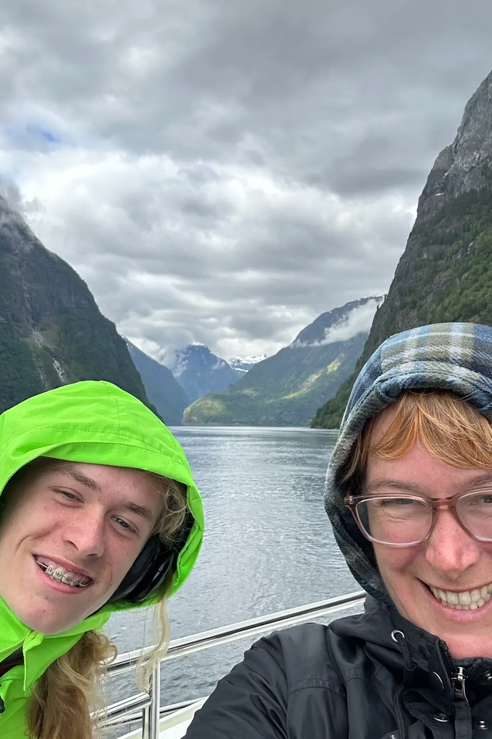 a teen boy and a woman smile on a boat on a Norwegian fjord with clouds in the background