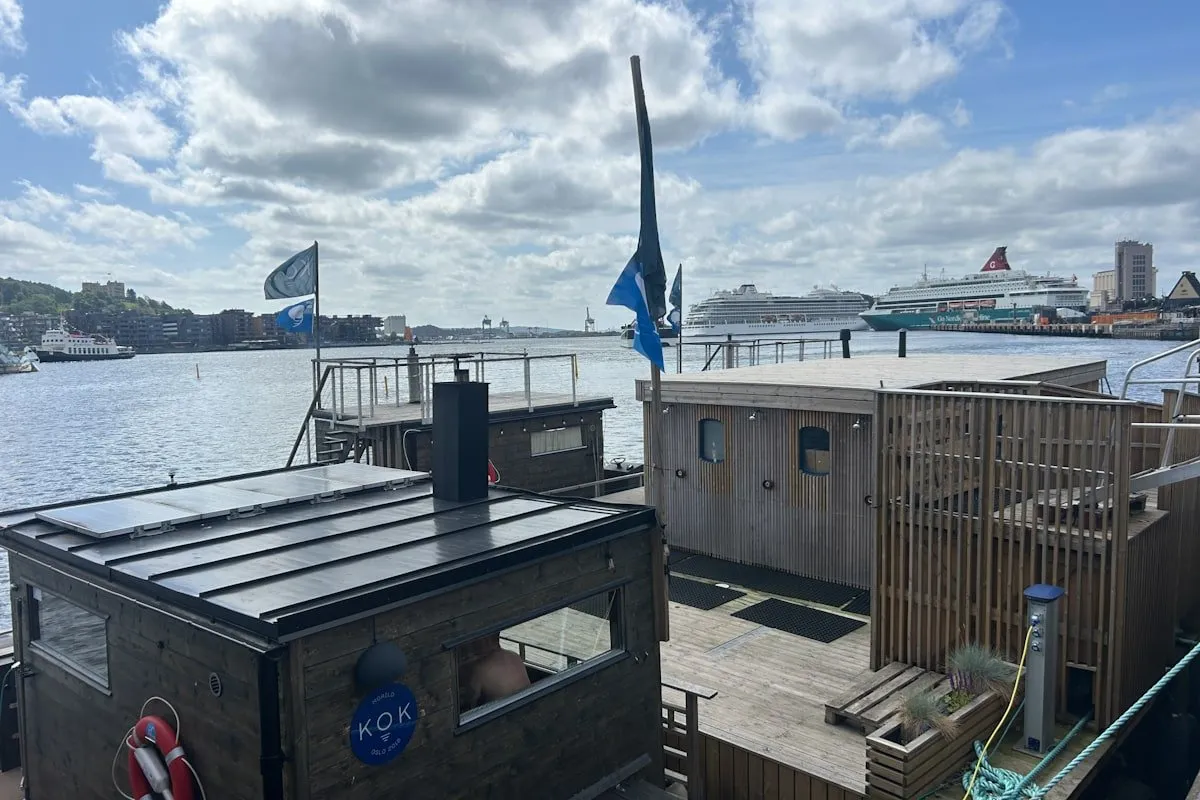 KOK Oslo floating sauna dock with blue flags overlooking fjord and cruise ship