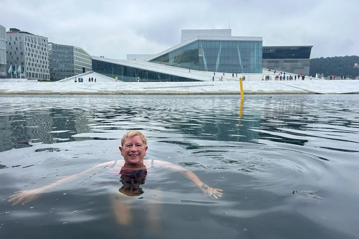 A smiling woman swims in Oslo harbor with Oslo Opera House architecture in background